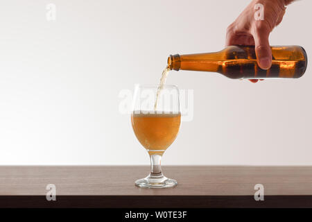 Hand holding Beer bottle filling a glass cup sur table en bois et fond blanc . Composition horizontale. Vue de face. Banque D'Images