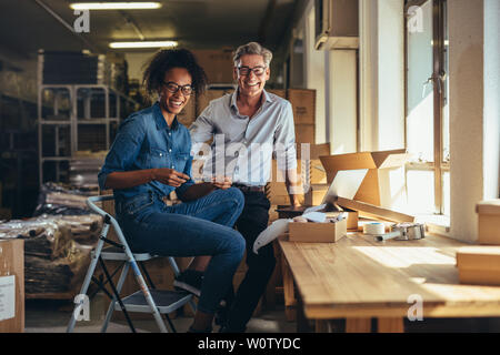 Smiling man and woman at boutique en ligne entrepôt. Succès de l'expédition de baisse des partenaires d'affaires. Banque D'Images