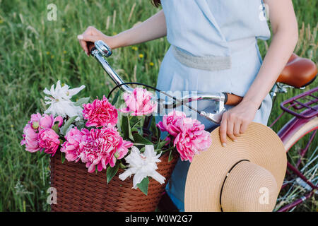 Images gros plan de belle femme mains tiennent un vélo avec un panier de fleurs rouges et blanches et d'un élégant chapeau sur le fond de la nature. Concept Banque D'Images