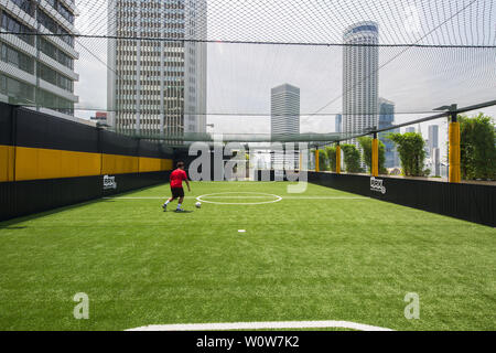 Au cours d'un après-midi ensoleillé, un homme en chemise rouge se rendant à un coup de pied à la balle dans le terrain de futsal au centre commercial Funan Mall, à Singapour Banque D'Images