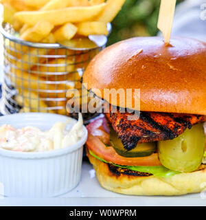 Burger de poulet cajun avec plaquettes de frites sur une table mise à l'été à l'extérieur. Banque D'Images