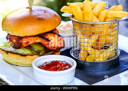 Burger de poulet cajun avec plaquettes de frites sur une table mise à l'été à l'extérieur. Banque D'Images