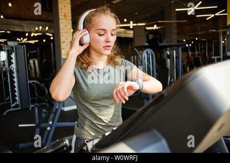 Fille termine la cardio- formation sur le tapis roulant et regarde sur sa montre. Banque D'Images