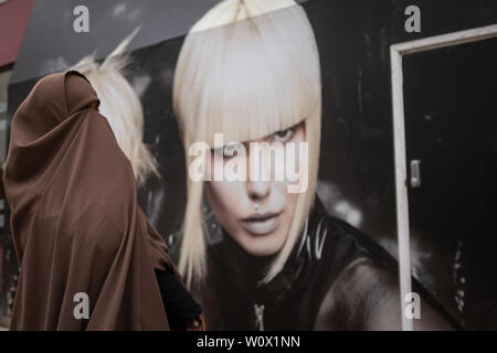 Bristol, UK, avril, 16, 2019 : Une jeune femme musulmane dans un hijab cache son visage alors qu'elle marche a adopté un panneau d'un mannequin blond avec Stark et hairc Banque D'Images