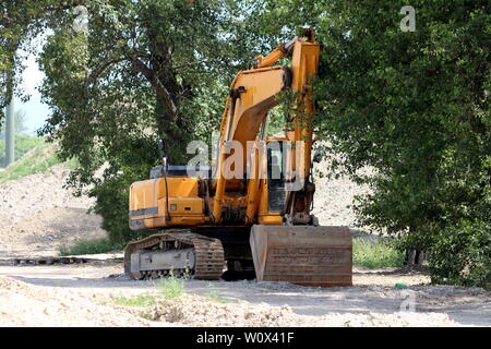 Parqué dans l'excavatrice ombre des grands arbres en attente pour les camions à charger au grand site en construction sur le printemps chaud et ensoleillé Banque D'Images