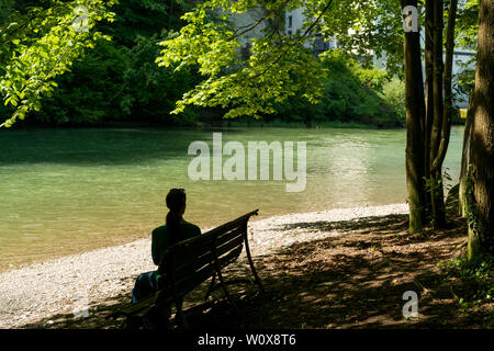 Vue horizontale d'une femme assise sur un banc à l'ombre des arbres sur une rivière idyllique Banque D'Images