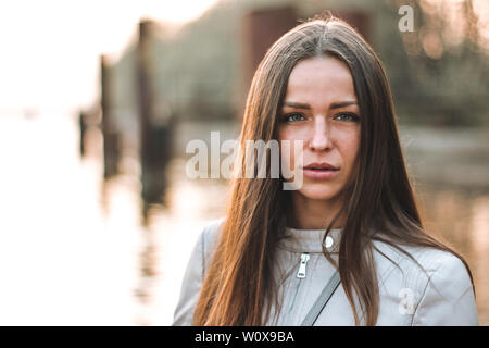 Portrait d'une belle jeune fille aux cheveux longs, de grands yeux gris dans une veste en cuir beige à directement à l'appareil photo. Coucher de soleil. Banque D'Images