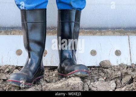 Des bottes en caoutchouc pour utilisation professionnelle. Un conducteur de pelle se distingue avec ses bottes de caoutchouc à l'avant de la drague de son godet bulldozer dans le sol agité. Banque D'Images