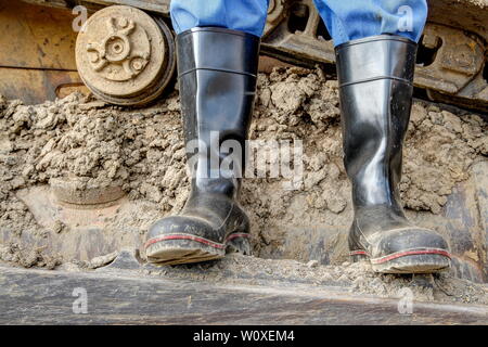 Des bottes en caoutchouc pour utilisation professionnelle. Un conducteur de pelle se distingue avec ses bottes en caoutchouc poussiéreux sur le dur chaint de son bulldozer. Banque D'Images