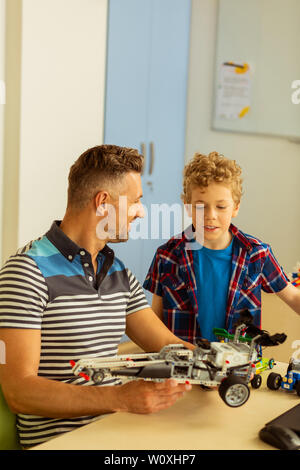 Notre travail. Positive joyeuse homme tenant un modèle de voiture tout en le rendant avec son fils Banque D'Images