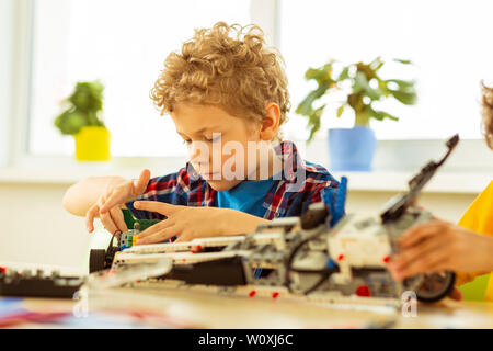 Être concentré. Cute blonde boy en se concentrant sur sa tâche pendant que la construction d'un modèle de voiture Banque D'Images