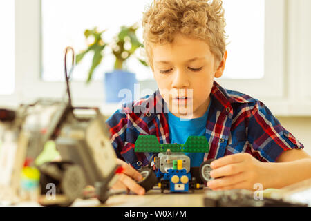 Faire une voiture modèle. Belle blonde boy holding toy roues dans ses mains tout en faisant un modèle de voiture Banque D'Images