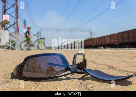 Les lunettes cassées sont à la gare, dans le contexte de l'adoption par le garçon en vélo et train en mouvement Banque D'Images