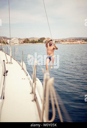 Jeune homme sauter de bateau à voile en mer. Banque D'Images