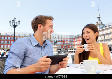 Les touristes de Madrid au café boire du café s'amusant à l'aide de tablet app voyage sur la Plaza Mayor. Tourist couple sightseeing visiter attractions et sites touristiques en Espagne. Jeune femme et l'homme Banque D'Images