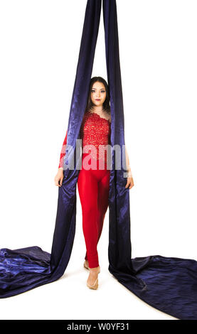 Une jeune femme aux cheveux longs en costume rouge effectue des exercices de gymnastique et de cirque sur la soie. Prise de vue en studio sur fond blanc, image isolée. Banque D'Images