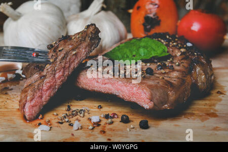 Steak au poivre moyen coupé en tranches sur la plaque en bois avec des épices assaisonnements dans ton sombre gris et l'éclairage. Banque D'Images