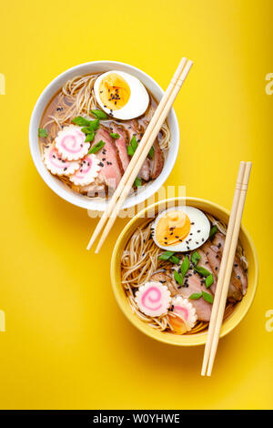 Deux bols de soupe aux nouilles ramen japonais avec bouillon de viande de porc, œufs, narutomaki, avec le jaune sur fond jaune pastel. Plat traditionnel du Japon Banque D'Images