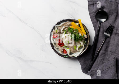 Soupe de nouilles asiatiques, avec la viande et les légumes dans un bol avec de la vaisselle et serviettes sur fond blanc. Vue supérieure horizontale, l'espace libre pour le texte Banque D'Images