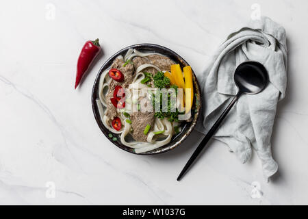 Soupe de nouilles asiatiques, avec la viande et les légumes dans un bol avec une serviette de table et gris sur fond blanc. Vue supérieure horizontale, l'espace libre pour le texte Banque D'Images