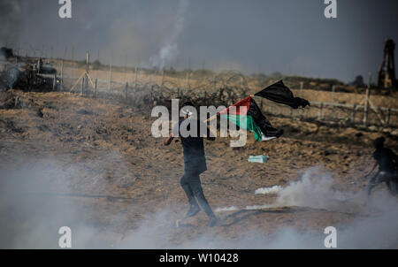 Manifestant palestinien avec un drapeau fuit de la fumée des gaz lacrymogènes tirés à leur égard pendant les affrontements.palestiniens se sont affrontés avec les forces israéliennes au cours d'une manifestation appelant à la levée du blocus israélien de Gaza et exigeante pour le droit de retourner dans leur patrie, à l'Israel-Gaza clôture frontalière dans le sud de la bande de Gaza. Banque D'Images