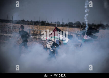 Manifestant palestinien avec un drapeau fuit de la fumée des gaz lacrymogènes tirés à leur égard pendant les affrontements.palestiniens se sont affrontés avec les forces israéliennes au cours d'une manifestation appelant à la levée du blocus israélien de Gaza et exigeante pour le droit de retourner dans leur patrie, à l'Israel-Gaza clôture frontalière dans le sud de la bande de Gaza. Banque D'Images