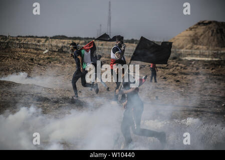 Manifestant palestinien avec un drapeau fuit de la fumée des gaz lacrymogènes tirés à leur égard pendant les affrontements.palestiniens se sont affrontés avec les forces israéliennes au cours d'une manifestation appelant à la levée du blocus israélien de Gaza et exigeante pour le droit de retourner dans leur patrie, à l'Israel-Gaza clôture frontalière dans le sud de la bande de Gaza. Banque D'Images