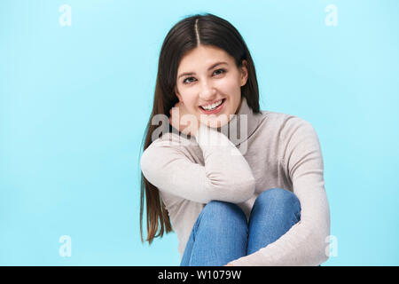 Studio portrait d'une jolie femme de race blanche, assis sur le plancher, smiling, isolé sur fond bleu Banque D'Images