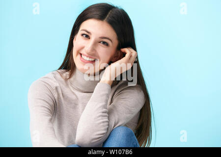 Studio portrait d'une jolie femme de race blanche, assis sur le plancher, smiling, isolé sur fond bleu Banque D'Images