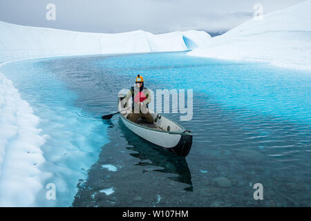 Sur un lac au-dessus de la Matanuska Glacier, un jeune homme d'une section peu profonde des palettes avec des pierres à la terre son canot. Banque D'Images