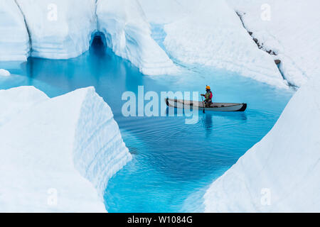 L'homme sur un canot flotte au-dessus d'une grotte de glace inondée dans une piscine d'un bleu profond tout en étant plu le en Alaska Banque D'Images
