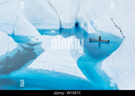 Sur le glacier Matanuska en Alaska, un guide d'escalade sur glace flotte un canoë gonflable sur un lac d'un bleu profond sur le glacier. Les étroits canyons inondés le Banque D'Images
