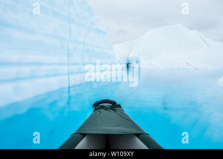 Déménagement en canoë à travers l'eau d'un lac glaciaire d'un bleu profond sur le dessus de la Matanuska Glacier en Alaska. Dans la distance est une petite grotte de glace sombre Banque D'Images