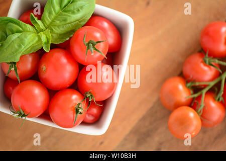 Tomates cerise bio cueillies fraîches avec des feuilles de basilic dans un plat carré blanc sur fond de bois. Concept de saine alimentation dans flatlay compositi Banque D'Images