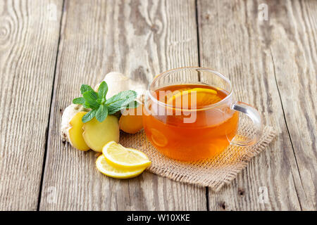 Un verre tasse de thé au citron, gingembre et menthe sur table rustique en bois. Banque D'Images