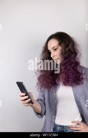 Jeune fille pensivement cherche dans Téléphone. Coloration des cheveux bouclés violet. Fond gris Banque D'Images