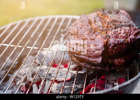 Un grand de poitrine et d'être sur un petit barbecue grill chaufferette avec braise en-dessous avec une sunburst. Banque D'Images