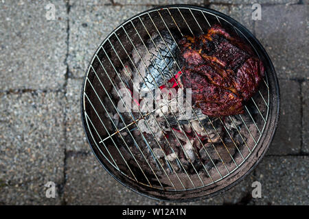 Une vue d'un grand de poitrine et d'être sur un petit barbecue grill chaufferette avec braise en dessous. Banque D'Images