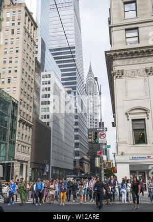 Des foules de gens attendent pour traverser la 5ème Avenue, sur la 42e rue, avec l'emblématique Chrysler Building à l'arrière-plan quelques blocs à l'Est. Banque D'Images