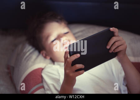 Little Boy using digital tablet la nuit dans la chambre Banque D'Images