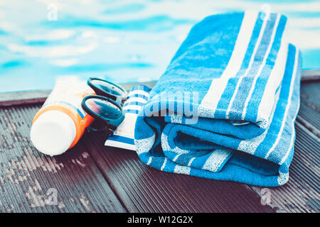 Lunettes de soleil, le tube de crème solaire, serviette bleu, proche piscine, fond tropical Banque D'Images