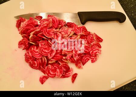 Frais de la ferme, en tranches, d'un rouge vif (betterave betterave chioggia) sur une planche à découper blanc, avec couteau, Wisconsin, USA. Banque D'Images