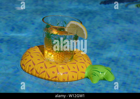 Ananas en plastique tasse d'eau avec une rondelle de citron, flottant dans un porte-boissons ananas gonflable dans une piscine. Banque D'Images