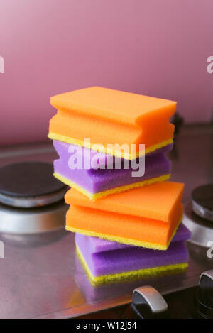 Une pile d'éponges violet et orange pour le lavage sur la cuisinière. La notion de ménage et nettoyage. Plusieurs éponges sur la plaque de cuisson. Banque D'Images