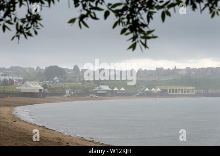Les trames du feuillage des arbres d'une vue sur la plage de sable de Barry Island qui est vide, mais pour un lointain lifeguard van, au cours d'une douche lourde. Banque D'Images