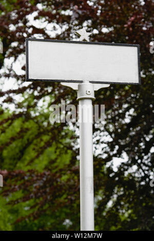 Vide vertical panneau blanc avec bordure noire sur un post avec une étoile sur le dessus contre un rouge foncé et vert feuille d'arbre arrière-plan flou Banque D'Images