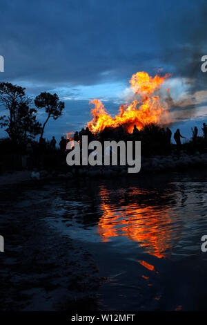 Feu de joie sur la plage à Nivaa Harbour en célébration de la mi-été et St. John's Eve. Flammes reflètent dans l'eau peu profonde dans l'Øresund. Banque D'Images