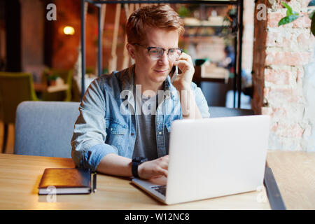 L'homme en chemise en jean types sur l'ordinateur portable et parle au téléphone. Banque D'Images