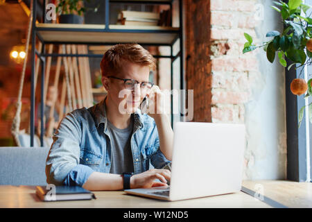 L'homme en chemise en jean types sur l'ordinateur portable et parle au téléphone. Banque D'Images