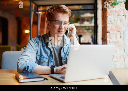 L'homme en chemise en jean types sur l'ordinateur portable et parle au téléphone. Banque D'Images